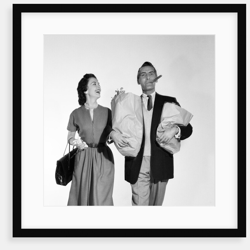 1950s couple walking woman smiling at man carrying grocery bags smoking cigar by Anonymous