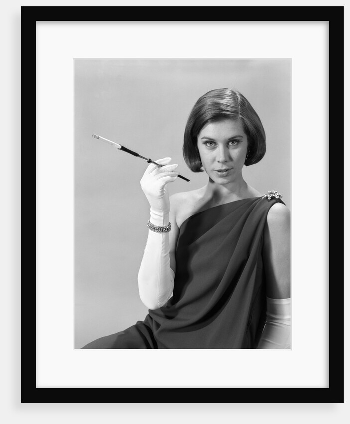 1960s formally elegantly dressed young woman looking at camera with a cigarette holder wearing long white gloves by Anonymous