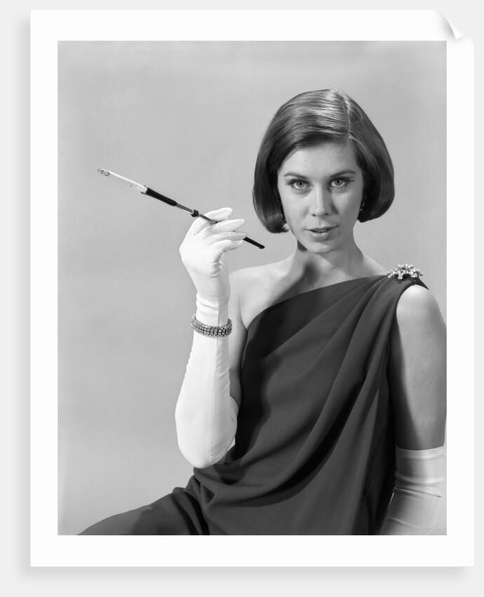 1960s formally elegantly dressed young woman looking at camera with a cigarette holder wearing long white gloves by Anonymous