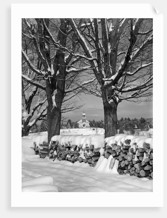 1940s pile of snow-covered firewood logs stacked between two trees with country church in background by Anonymous