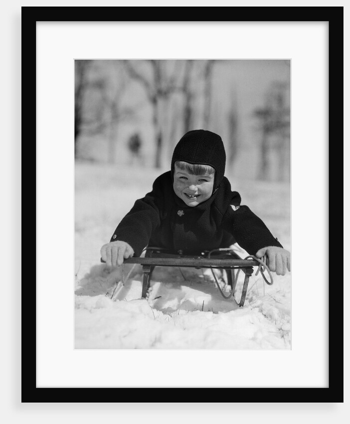 1930s young smiling boy on sled in snow looking at camera by Anonymous