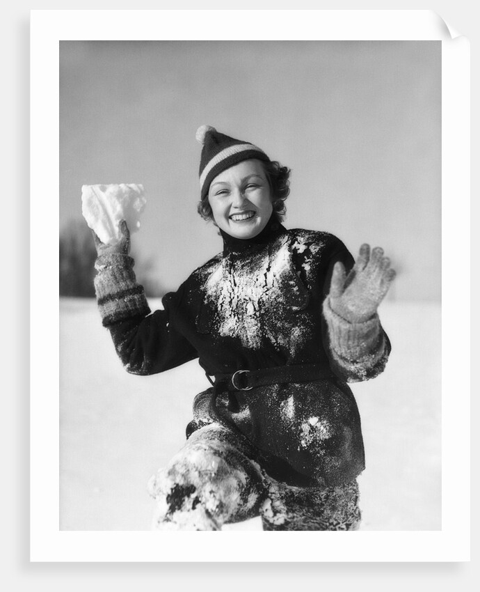 1930s smiling young woman covered in snow throwing piece of snow squinting looking at camera by Anonymous