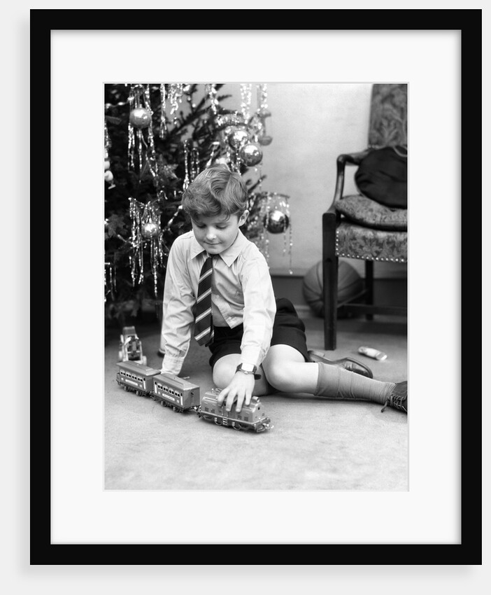 1930s young boy playing with toy train by christmas tree by Anonymous