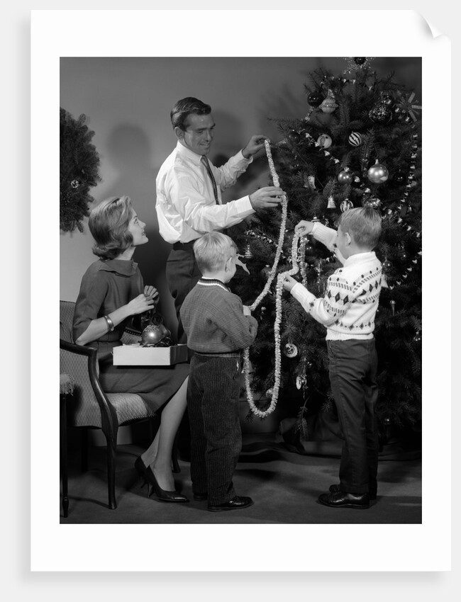 1960s family father mother two sons trimming christmas tree with string of popcorn by Anonymous