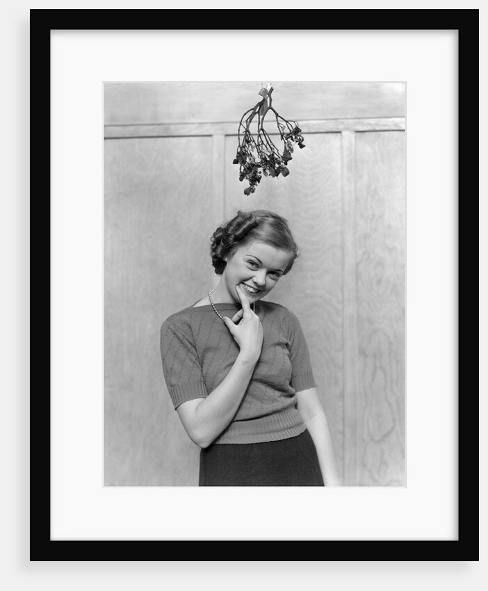 1930s 1940s cute young woman standing under mistletoe smiling hand near mouth looking at camera by Anonymous