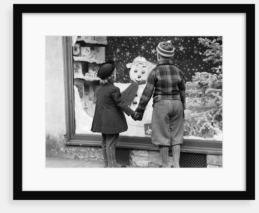 1930s back view boy and girl holding hands looking at decorated christmas window by Anonymous
