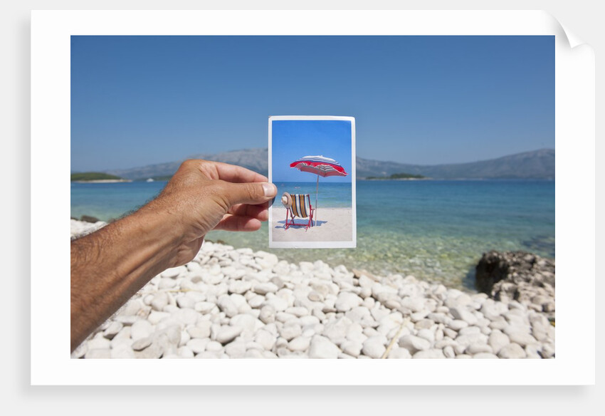 Hand holding photograph depicting deck chair and sunshade, Lumbarda, Korcula island, Croatia by Anonymous