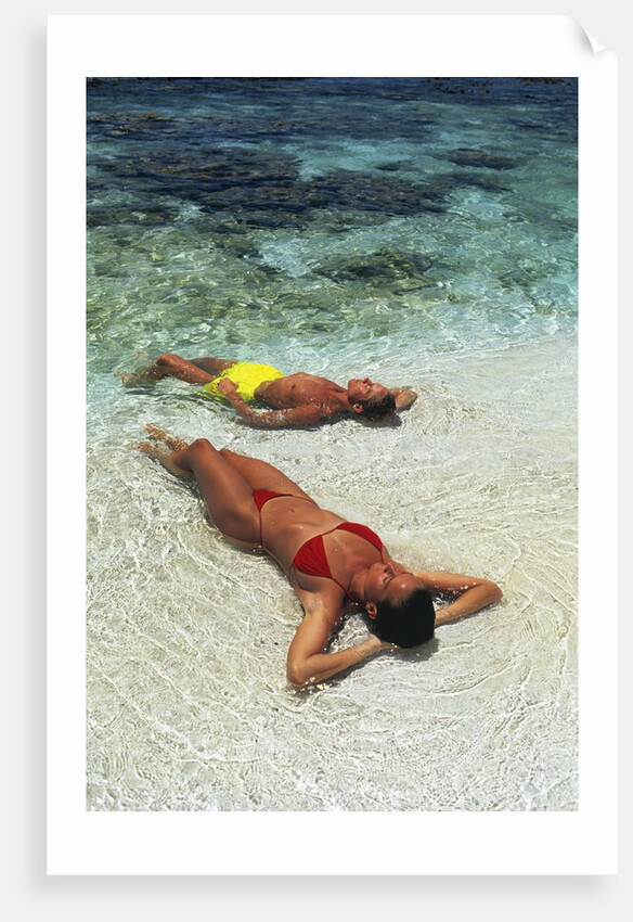 1990s Couple Sunbathing In Shallow Water At The Ocean's Edge by Anonymous