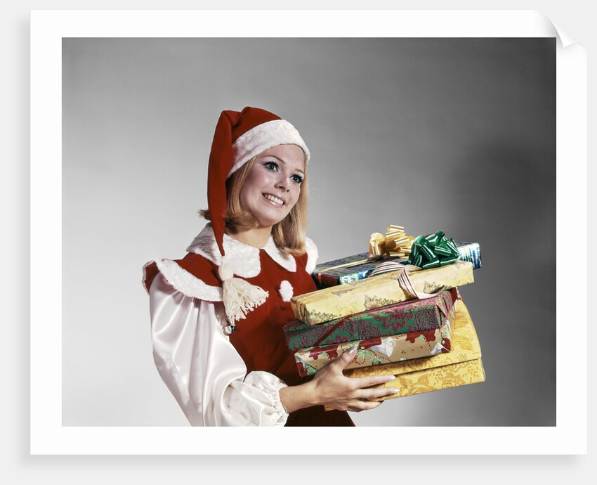1960s Young Woman In Red And White Santa Helper Costume And Hat Holding Pile Of Wrapped Christmas Presents Studio by Anonymous