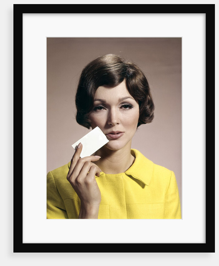 1960s Brunette Woman Holding Blank Business Card To Face Looking At Camera Wearing Yellow Top by Anonymous