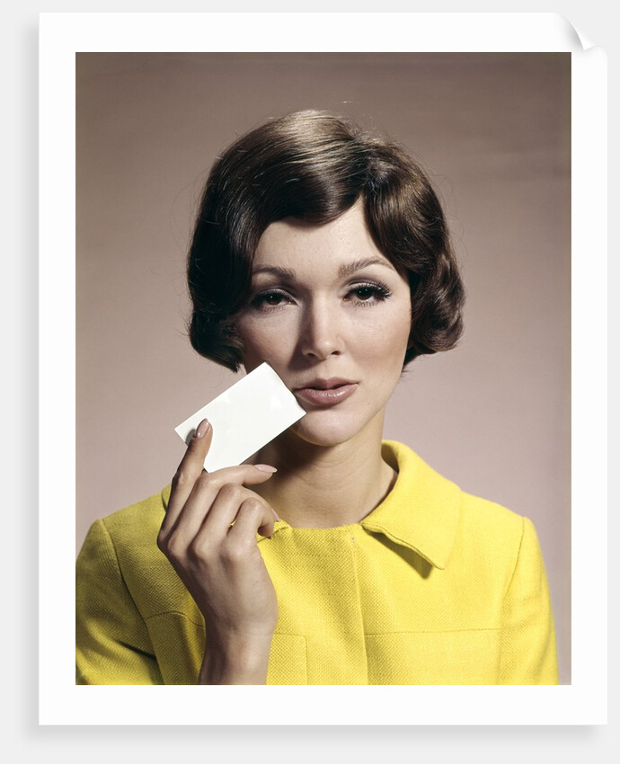 1960s Brunette Woman Holding Blank Business Card To Face Looking At Camera Wearing Yellow Top by Anonymous