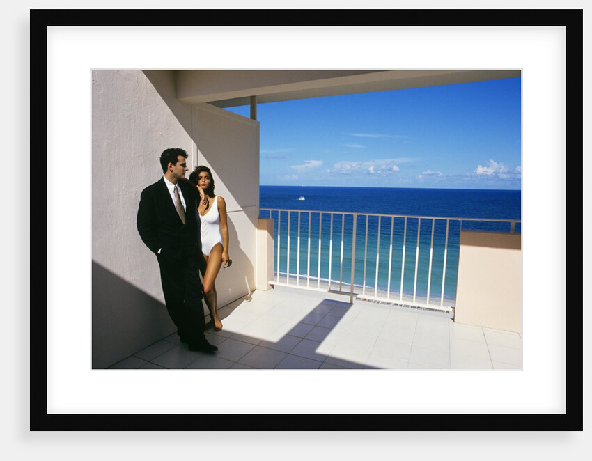 1990s Man In Dark Suit And Tie And Woman In White One Piece Bathing Suit Standing Together On Ocean Side Sun Deck by Anonymous