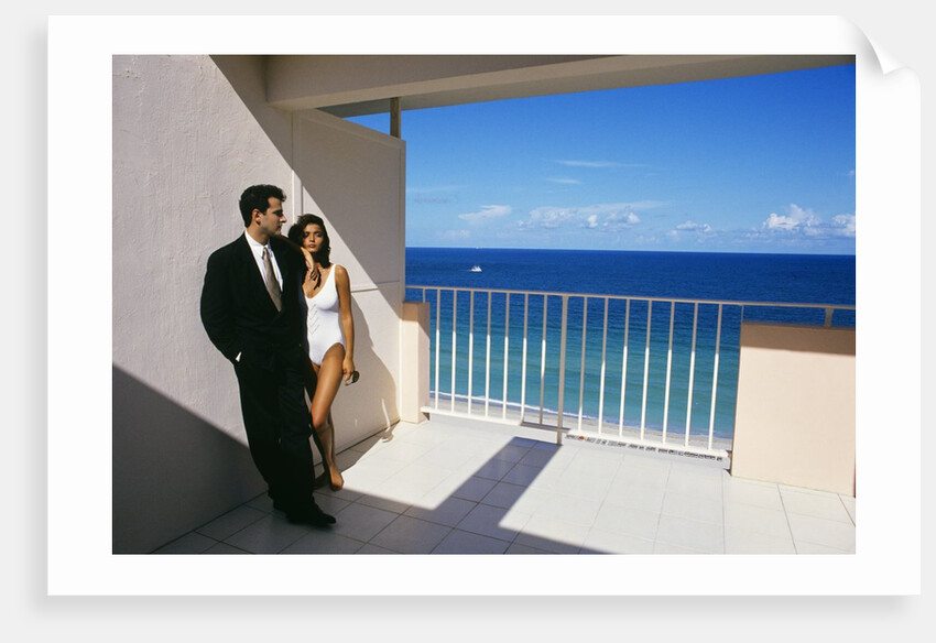 1990s Man In Dark Suit And Tie And Woman In White One Piece Bathing Suit Standing Together On Ocean Side Sun Deck by Anonymous