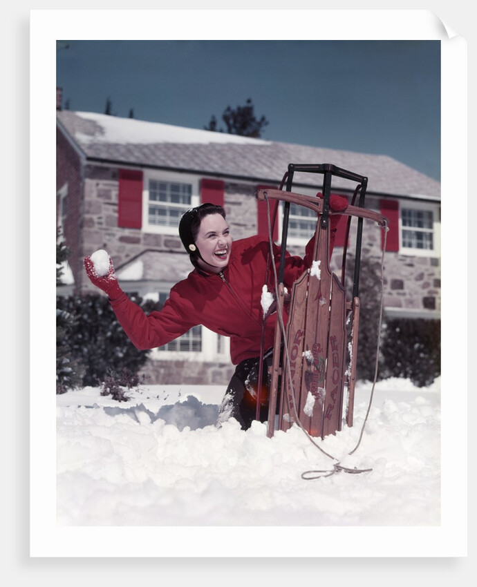 1950s Woman Hiding Behind Sled Throwing Snowball Front Stone House by Anonymous