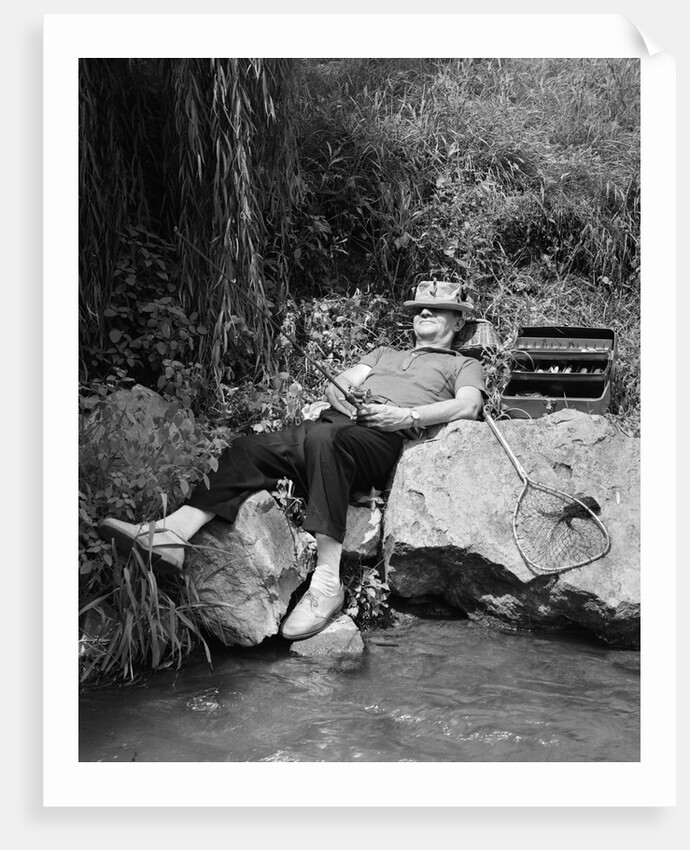 1950s Lazy Fisherman Lying Back On Rock With Hat Pulled Over Eyes Fishing In Creek by Anonymous