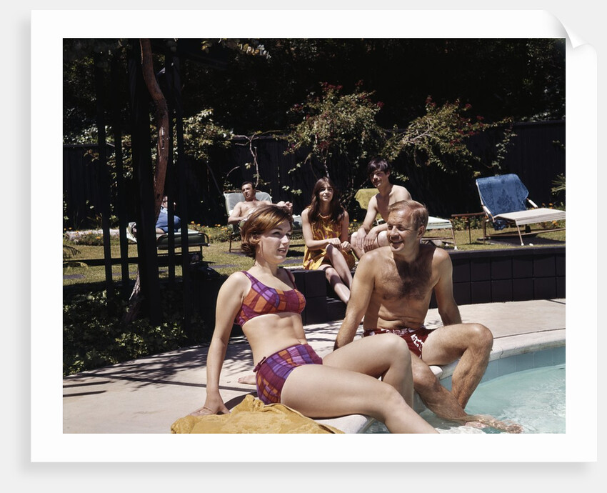 1960s Four People On Patio Couple Man Woman Sitting On Edge Of Swimming Pool by Anonymous