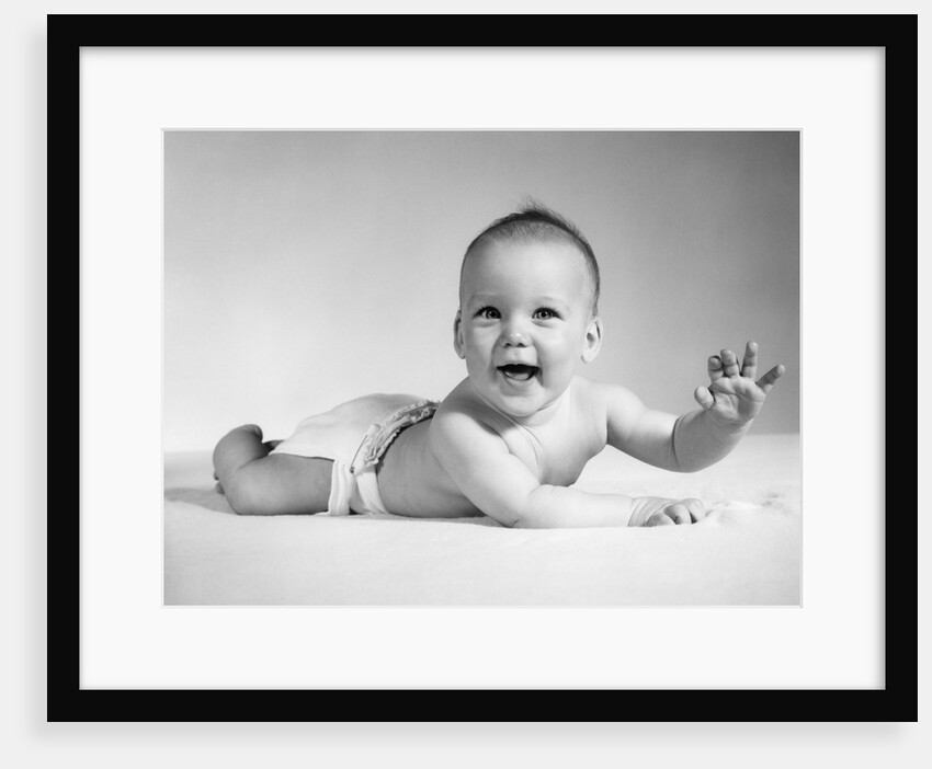 1960s Smiling Baby Wearing Cloth Diaper Lying On Stomach Looking At Camera Arm Raised by Anonymous