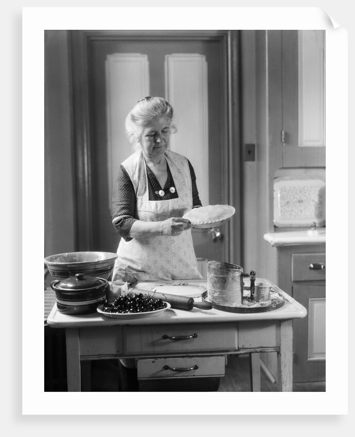 1920s 1930s Senior Woman Grandmother Wearing Apron Crimping Crust Making A Cherry Pie In Kitchen by Anonymous