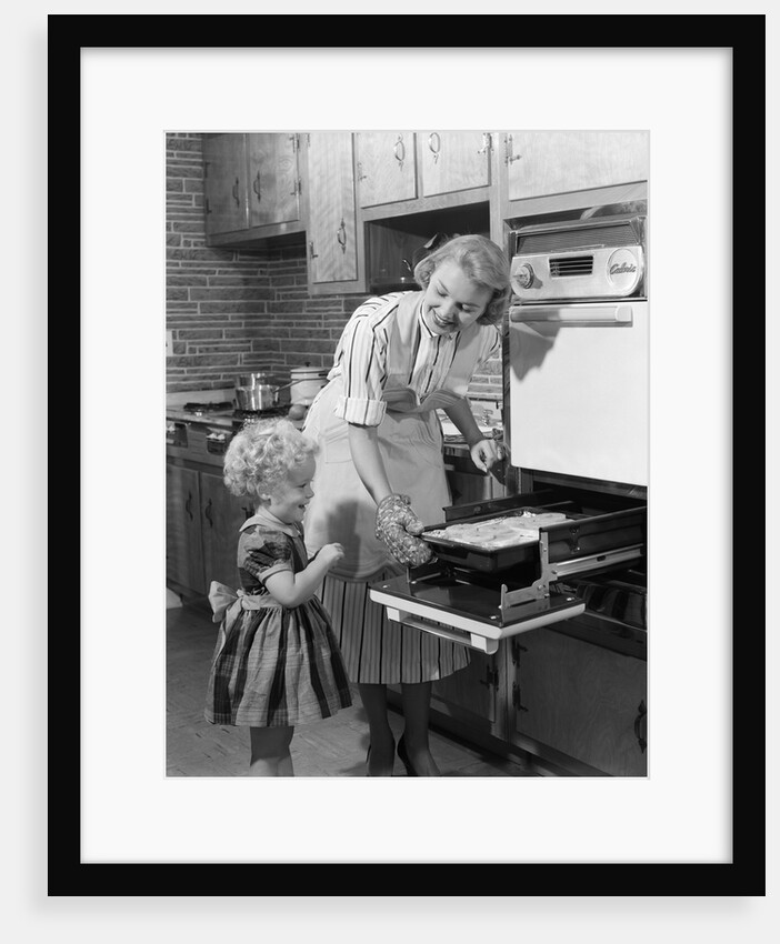 1950s Smiling Mother Daughter In Kitchen Broiling Pork Chops by Anonymous