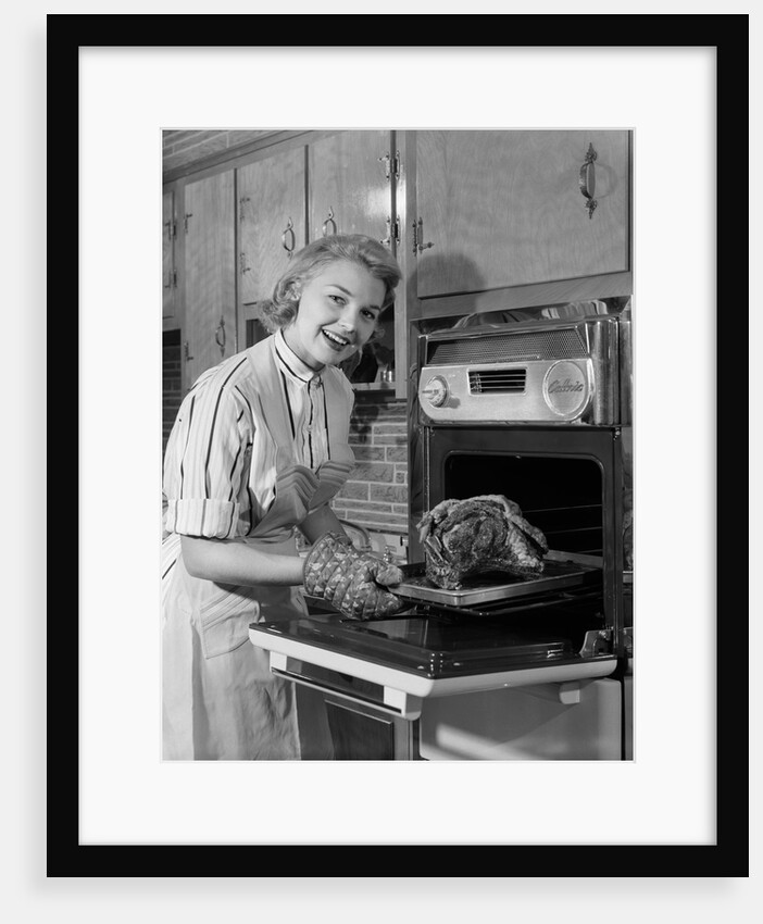1950s Smiling Woman Housewife Wearing Apron Taking Large Roast Beef From Electric Oven In Kitchen Looking At Camera by Anonymous
