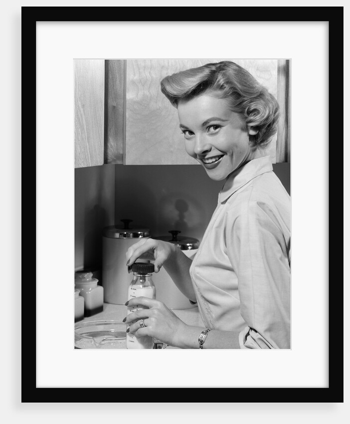 1950s Smiling Blonds Woman Mother Warming A Baby Bottle Of Milk In Kitchen Looking At Camera by Anonymous