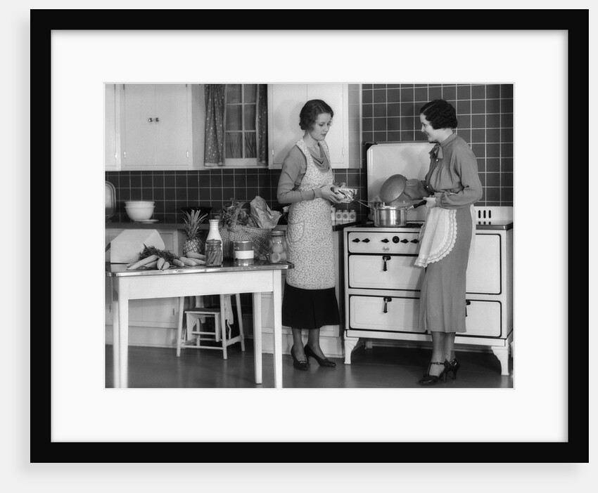 1930s Woman Housewife And Friend Wearing Apron Cooking Food In Kitchen On Gas Stove Indoor by Anonymous