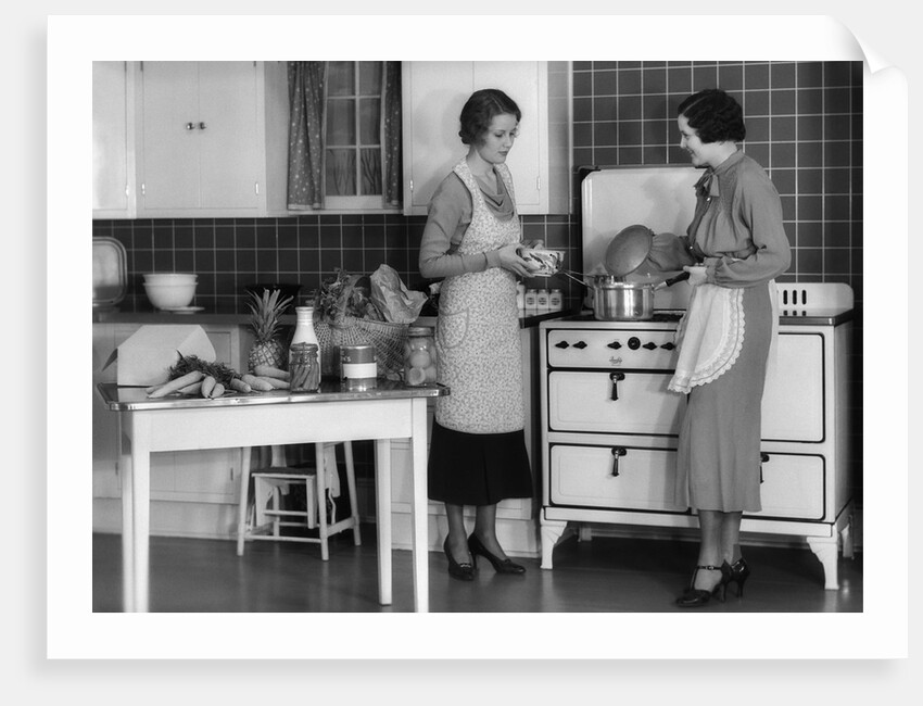1930s Woman Housewife And Friend Wearing Apron Cooking Food In Kitchen On Gas Stove Indoor by Anonymous