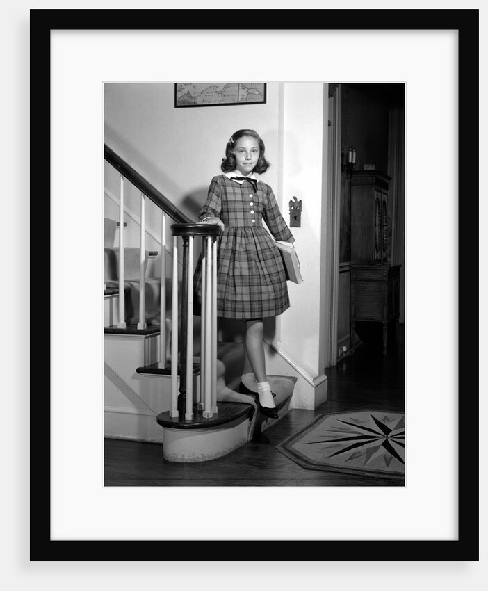 1950s Teenage Girl In Plaid Dress And White Ankle Socks On Stairway Holding Banister Carrying School Books Looking At Camera by Anonymous