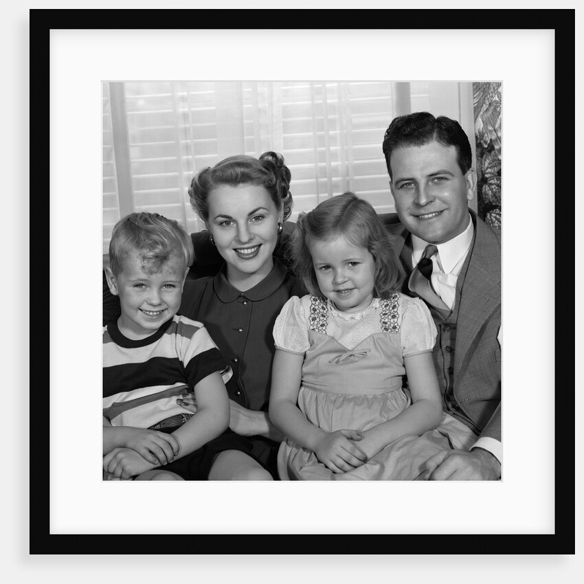 1940s 1950s Portrait Of Smiling Family Man Woman Boy Girl Sitting On Sofa Looking At Camera by Anonymous