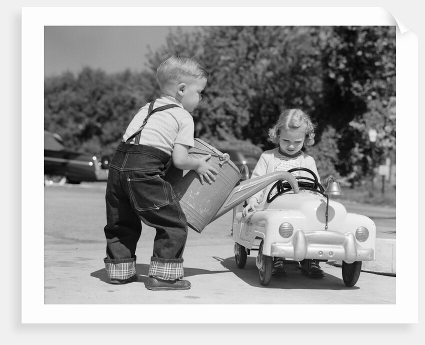 1950s Little Boy Playing Gas Station Pouring Water Into Toy Car For Little Girl by Anonymous