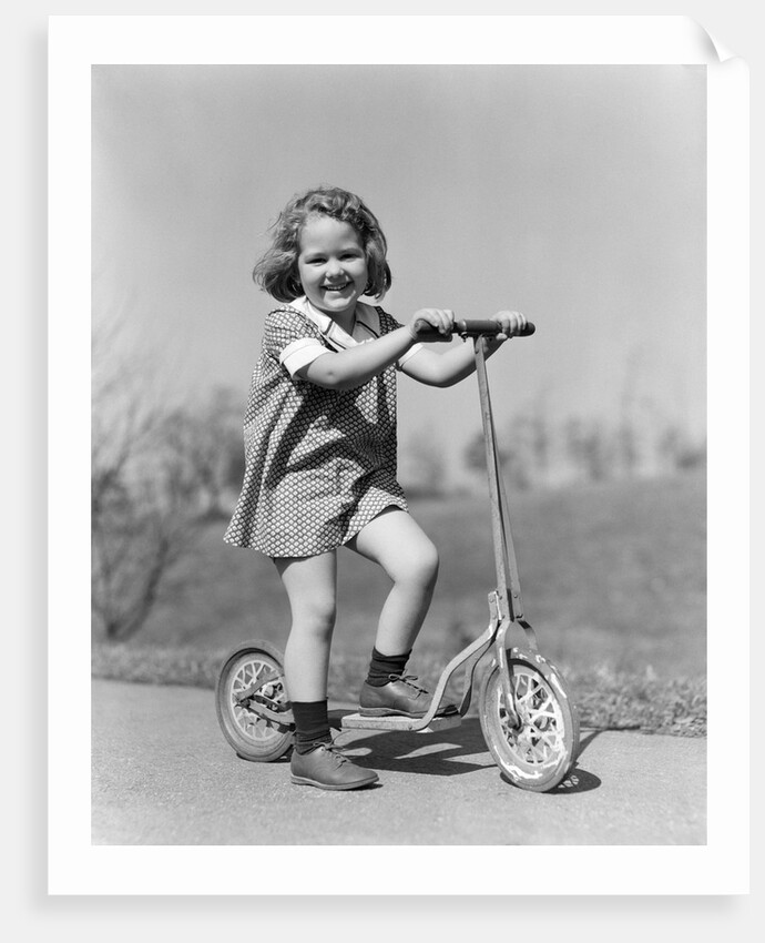 1930s Smiling Girl Playing On Scooter On Sidewalk Looking At Camera by Anonymous