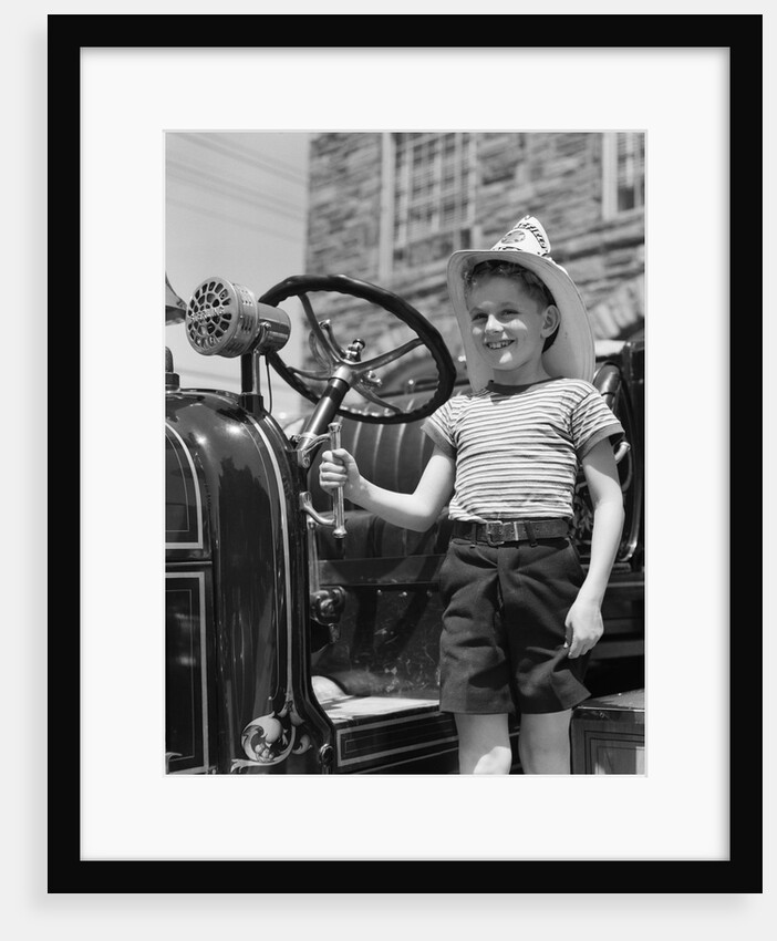 1930s Smiling Boy Standing Next To Fire Engine Wearing Firemans Hat by Anonymous