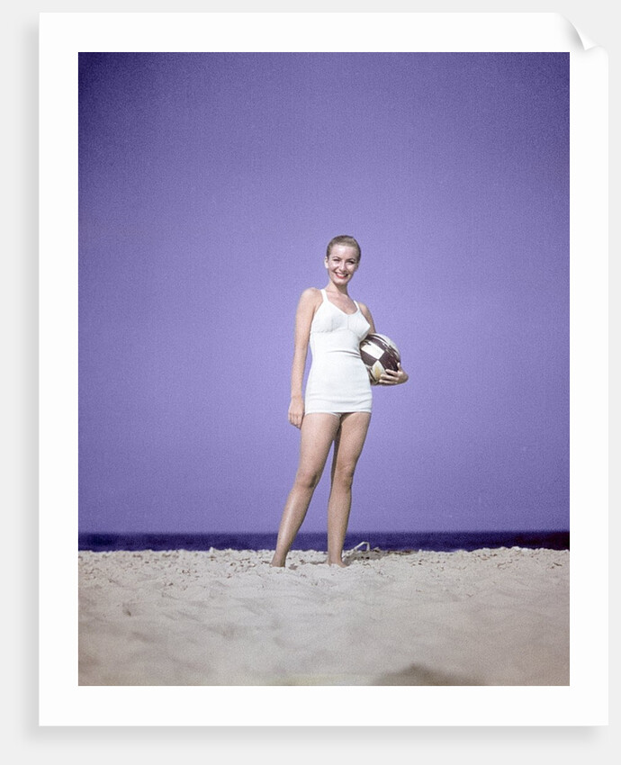 1950s Full Length Portrait Woman Light Blue One Piece Bathing Suit Swim Wear Standing On Sand Holding Beach Ball Fashion by Anonymous