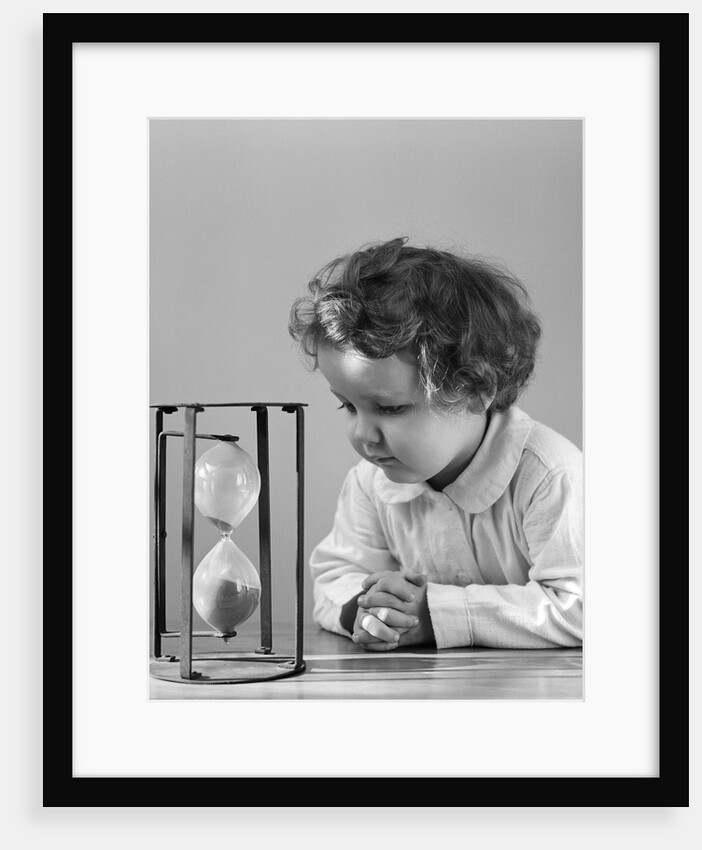 1940s young girl leaning on table staring at hourglass by Anonymous