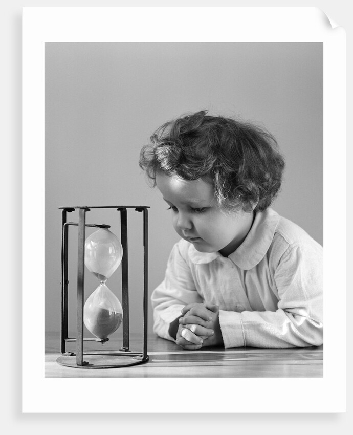 1940s young girl leaning on table staring at hourglass by Anonymous