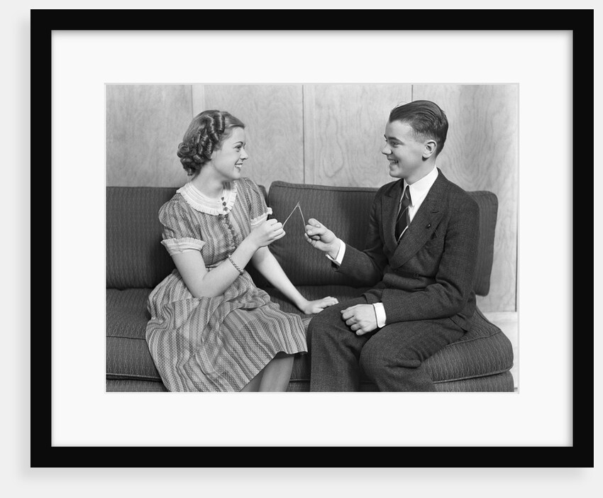 1930s teen boy and girl sitting on a sofa holding wishbone by Anonymous