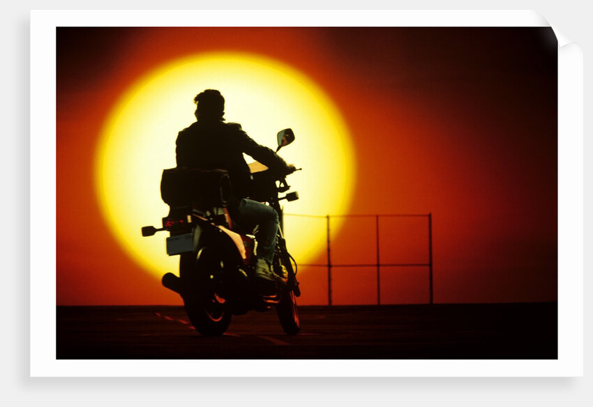 1980s silhouette of anonymous man on motorcycle driving toward rising setting sun by Anonymous