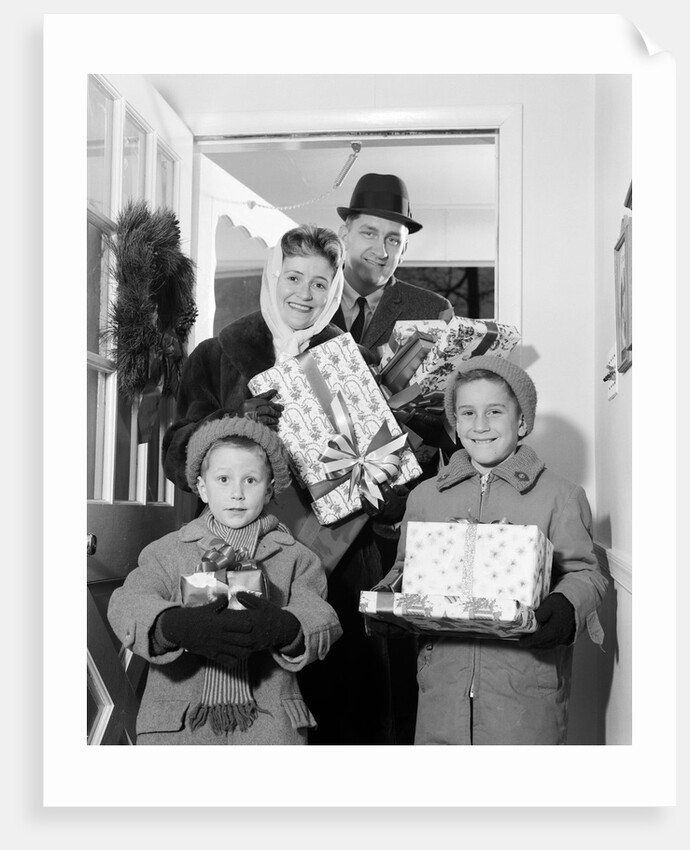 1960s family standing in doorway wearing winter coats and holding Christmas presents by Anonymous