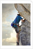Young man rock climbing up a vertical cliff by Anonymous