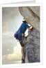 Young man rock climbing up a vertical cliff by Anonymous