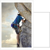 Young man rock climbing up a vertical cliff by Anonymous