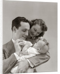 1940s Father Cradling Baby Daughter Feeding Her Bottle With Mother Looking Over His Shoulder by Anonymous