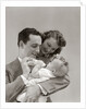 1940s Father Cradling Baby Daughter Feeding Her Bottle With Mother Looking Over His Shoulder by Anonymous