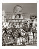 1960s Baby Sitting In Supermarket Cart Full Of Cans Eating Candy Bar With A Messy Face by Anonymous