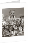 1960s Baby Sitting In Supermarket Cart Full Of Cans Eating Candy Bar With A Messy Face by Anonymous