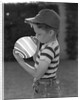 1950s Side View Of Boy In Baseball Cap and Striped T-Shirt Blowing Up Swirled Balloon by Anonymous