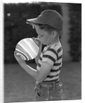 1950s Side View Of Boy In Baseball Cap and Striped T-Shirt Blowing Up Swirled Balloon by Anonymous