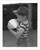 1950s Side View Of Boy In Baseball Cap and Striped T-Shirt Blowing Up Swirled Balloon by Anonymous