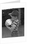 1950s Side View Of Boy In Baseball Cap and Striped T-Shirt Blowing Up Swirled Balloon by Anonymous