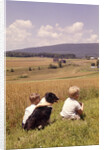 1960s Back Of Two Boys With Black And White Dog Sitting Hillside Field Looking Down To Farm by Anonymous